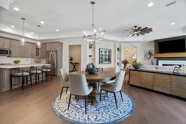 dining area with ornamental molding, ceiling fan with notable chandelier, dark hardwood / wood-style floors, and a tray ceiling