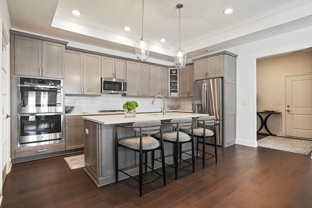 kitchen with pendant lighting, a center island with sink, decorative backsplash, dark hardwood / wood-style flooring, and stainless steel appliances