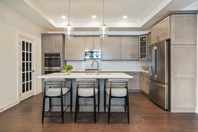 kitchen with stainless steel appliances, dark wood-type flooring, sink, decorative light fixtures, and an island with sink