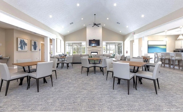 carpeted dining room featuring ceiling fan, a large fireplace, high vaulted ceiling, and a textured ceiling