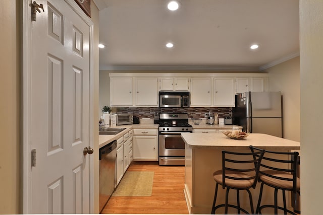 kitchen with decorative backsplash, appliances with stainless steel finishes, crown molding, white cabinets, and light hardwood / wood-style floors