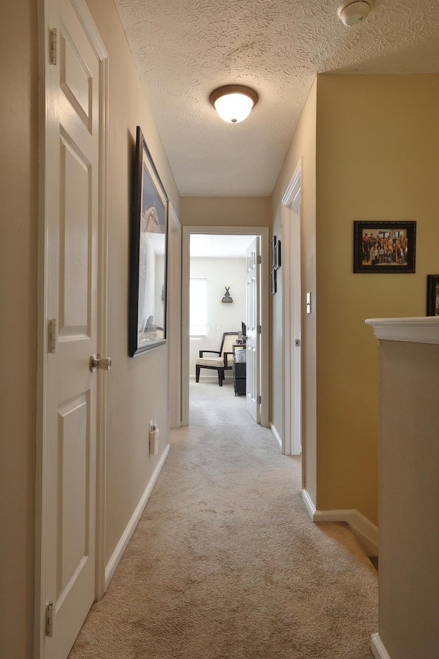 corridor with a textured ceiling and light carpet