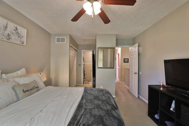 bedroom featuring ceiling fan, ensuite bathroom, light colored carpet, and a textured ceiling