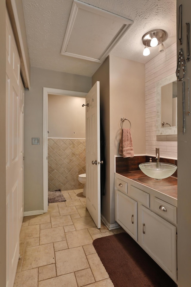 bathroom with a textured ceiling, vanity, toilet, and tile walls