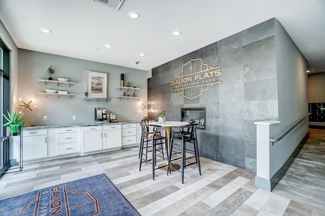 interior space with white cabinets, light stone countertops, tile walls, and light hardwood / wood-style flooring