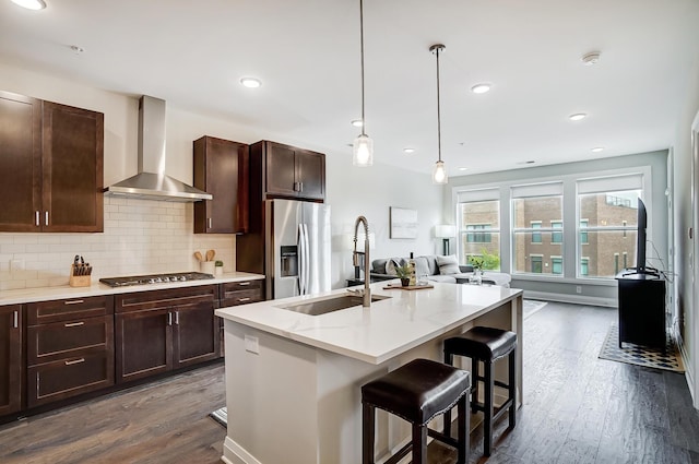 kitchen featuring a kitchen breakfast bar, wall chimney exhaust hood, stainless steel appliances, a center island with sink, and decorative light fixtures