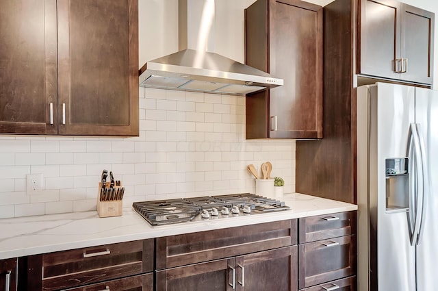 kitchen with backsplash, wall chimney exhaust hood, light stone countertops, dark brown cabinets, and stainless steel appliances