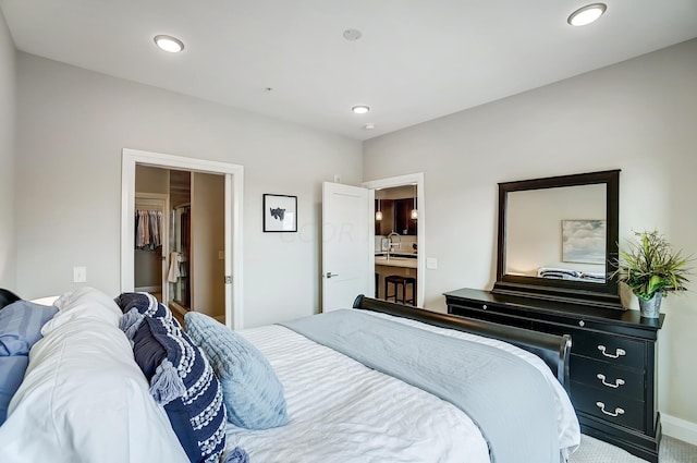 carpeted bedroom featuring ensuite bathroom, a walk in closet, and sink