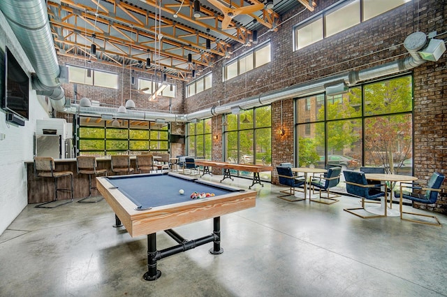 game room with brick wall, a towering ceiling, billiards, and concrete floors