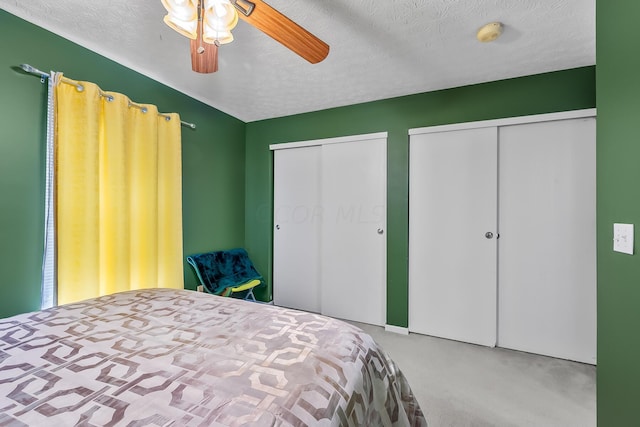 carpeted bedroom featuring ceiling fan, a textured ceiling, and two closets