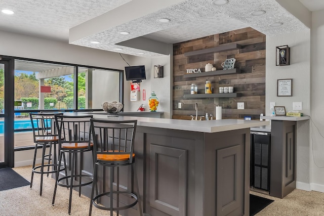 bar with dark brown cabinetry, a textured ceiling, beverage cooler, and wood walls