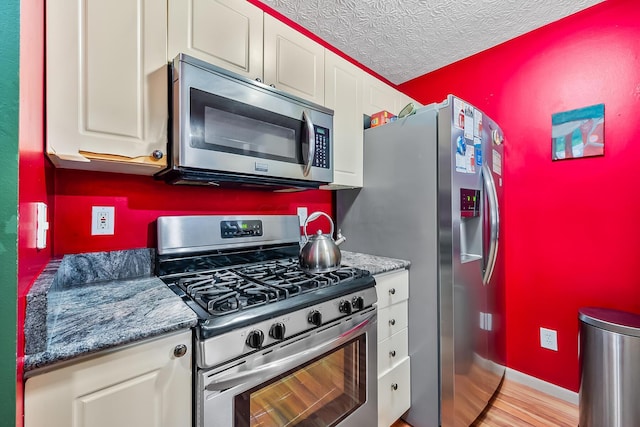 kitchen featuring white cabinets, stainless steel appliances, dark stone counters, and a textured ceiling