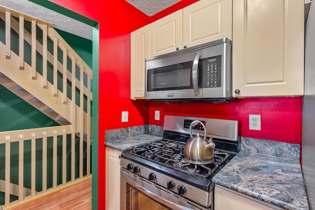 kitchen with a textured ceiling, light hardwood / wood-style floors, stainless steel appliances, and dark stone counters