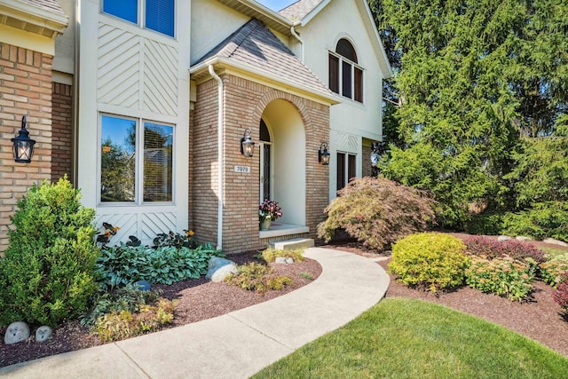 property entrance featuring brick siding, stucco siding, and a shingled roof