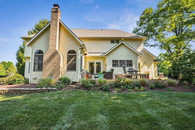 back of property with stucco siding, french doors, a chimney, and a yard