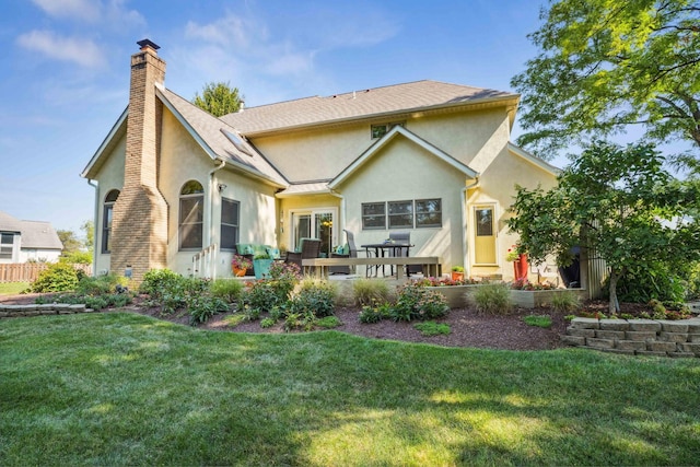 rear view of property with stucco siding, a yard, and a chimney