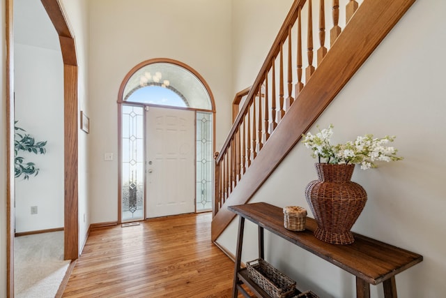 foyer entrance with stairway, a high ceiling, baseboards, and light wood finished floors