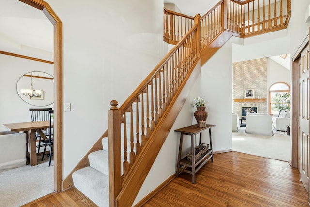 staircase featuring wood finished floors, an inviting chandelier, a fireplace, baseboards, and a towering ceiling