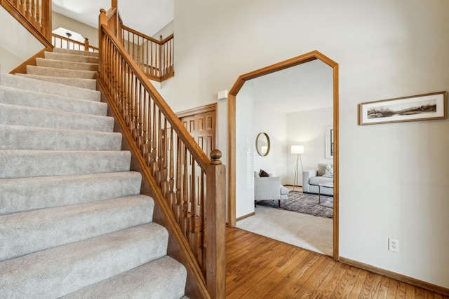 stairway featuring baseboards, wood finished floors, and a towering ceiling