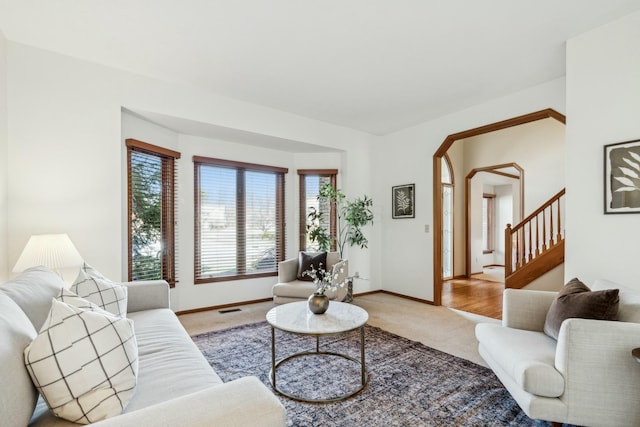 living room with visible vents, baseboards, stairs, light carpet, and arched walkways