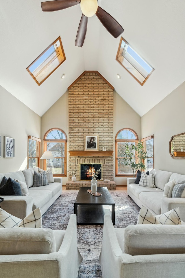 living room featuring a ceiling fan, a skylight, a fireplace, and high vaulted ceiling