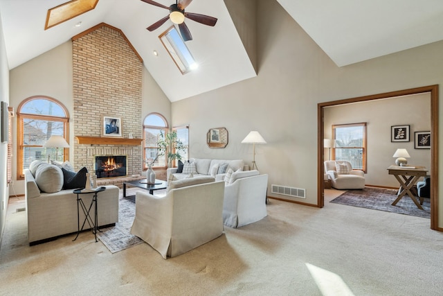 carpeted living area featuring visible vents, high vaulted ceiling, a ceiling fan, a skylight, and a fireplace