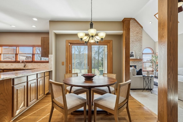 dining space featuring lofted ceiling, recessed lighting, light wood-style flooring, a fireplace, and a notable chandelier