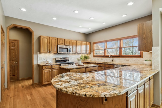 kitchen with a sink, stainless steel appliances, light wood-style floors, brown cabinetry, and light stone countertops