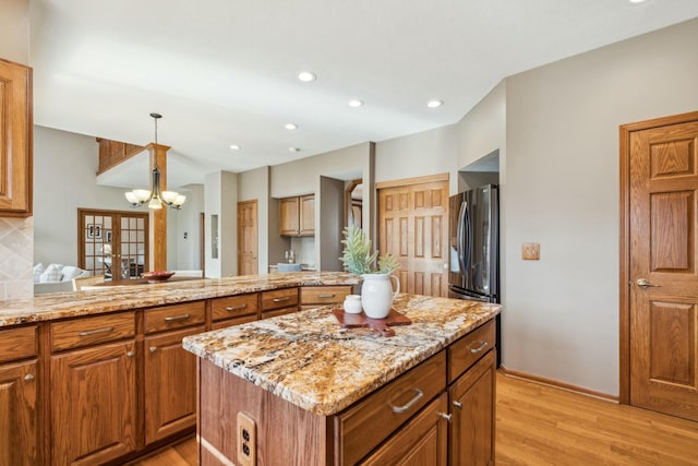 kitchen with brown cabinetry, light stone countertops, light wood-style floors, stainless steel fridge, and a center island