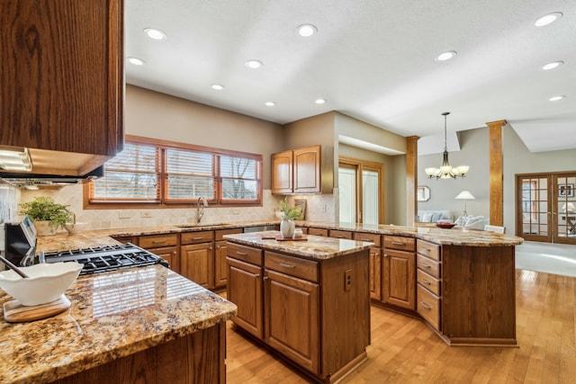 kitchen featuring light wood-type flooring, a sink, light stone counters, a kitchen island, and decorative backsplash