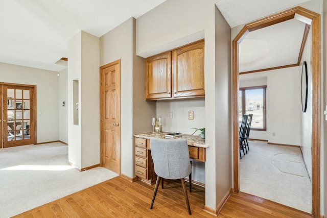 home office featuring light carpet, built in study area, light wood-type flooring, and baseboards