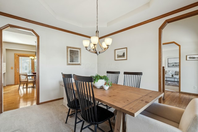 dining area with a raised ceiling, a notable chandelier, arched walkways, light wood finished floors, and baseboards