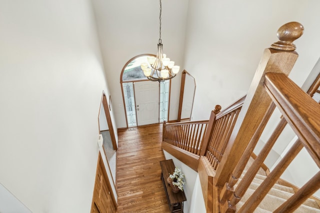 entryway featuring wood finished floors, baseboards, an inviting chandelier, a high ceiling, and stairs