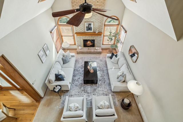 living room featuring baseboards, high vaulted ceiling, a brick fireplace, and a ceiling fan