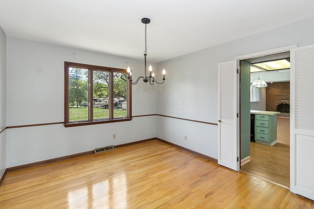 unfurnished room with an inviting chandelier, light hardwood / wood-style floors, and a brick fireplace