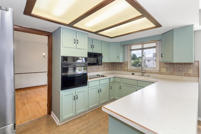 kitchen featuring light wood-type flooring, sink, backsplash, and black appliances