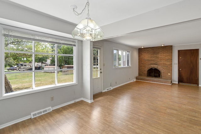 unfurnished living room featuring a fireplace, wood-type flooring, an inviting chandelier, and plenty of natural light