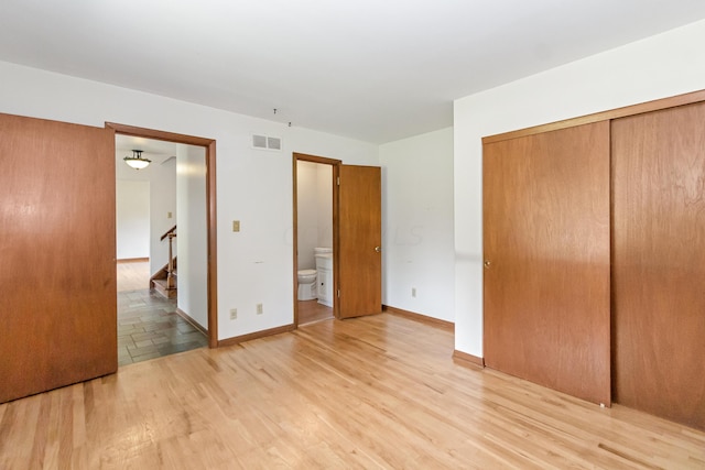 unfurnished bedroom featuring ensuite bathroom, a closet, and light hardwood / wood-style flooring