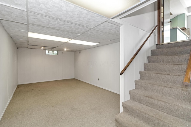 basement with a paneled ceiling and carpet