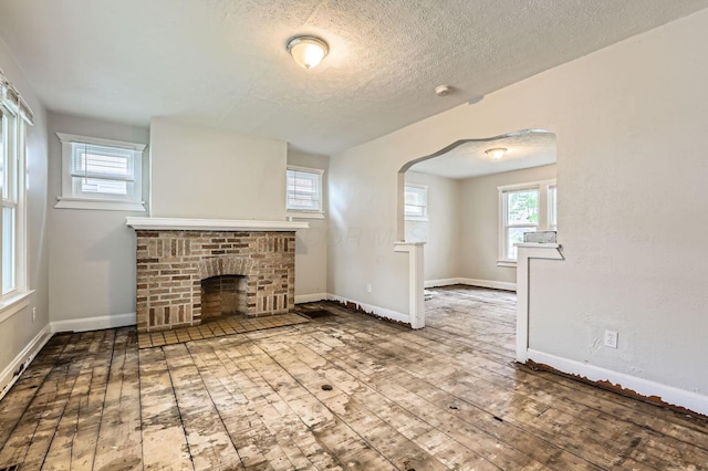 737 S Richardson Ave, Columbus, OH 43204 - unfurnished living room with a brick fireplace, arched walkways, healthy amount of natural light, hardwood / wood-style floors, and a textured ceiling