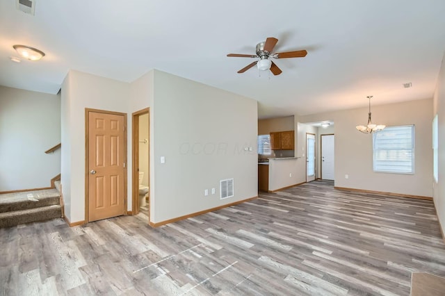 unfurnished living room with stairs, light wood-style floors, visible vents, and ceiling fan with notable chandelier