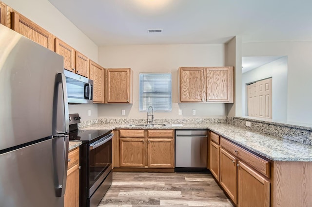 kitchen with a sink, a peninsula, stainless steel appliances, visible vents, and light wood-style flooring