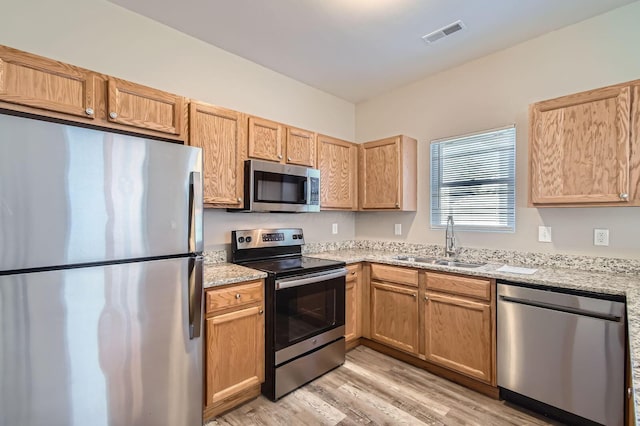 kitchen featuring light wood finished floors, a sink, visible vents, appliances with stainless steel finishes, and light stone counters