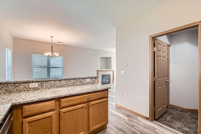 kitchen with a tile fireplace, pendant lighting, a notable chandelier, baseboards, and light stone counters