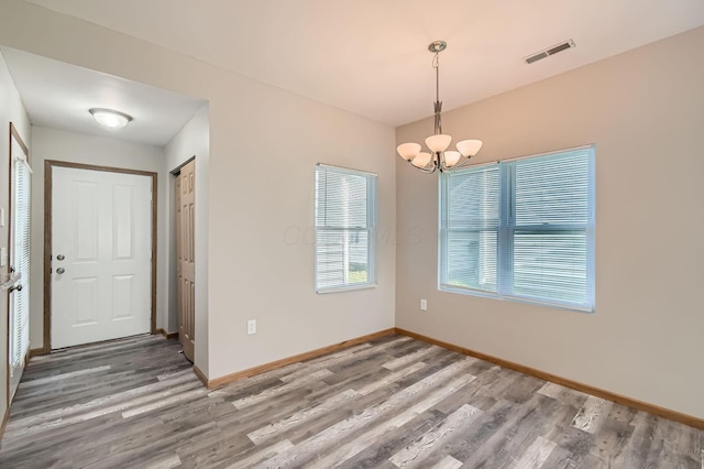 unfurnished dining area with an inviting chandelier, baseboards, visible vents, and wood finished floors