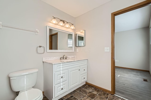 bathroom with baseboards, toilet, vanity, and visible vents