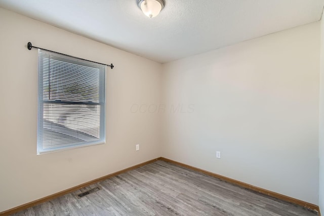 unfurnished room featuring visible vents, wood finished floors, and baseboards
