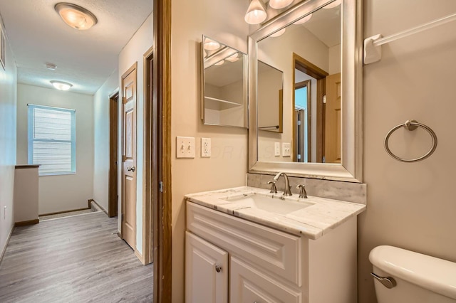 bathroom with toilet, baseboards, wood finished floors, and vanity