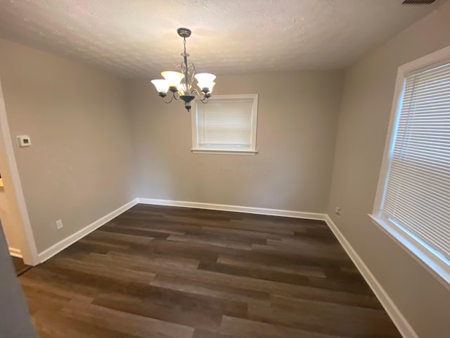 unfurnished dining area with a textured ceiling, an inviting chandelier, and dark wood-type flooring