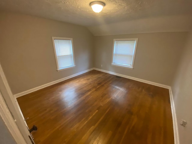 empty room featuring a textured ceiling, lofted ceiling, and dark wood-type flooring